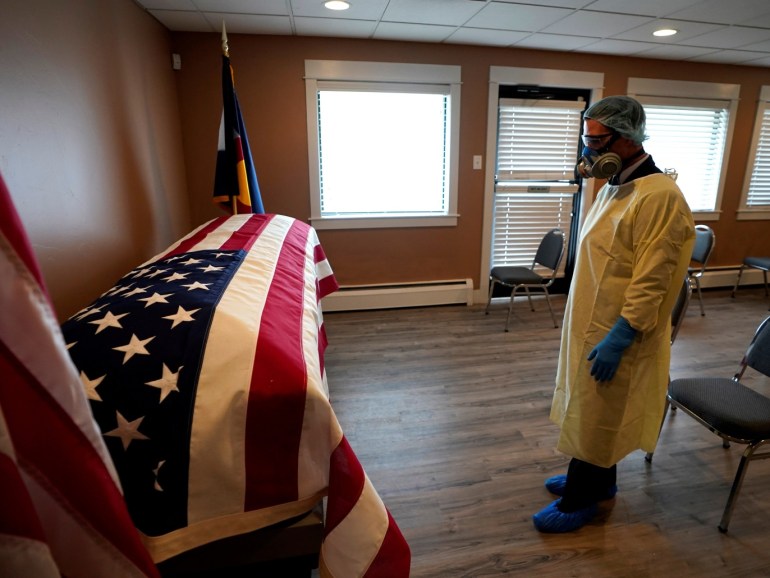Michael Neel, funeral director of of All Veterans Funeral and Cremation, wearing full PPE, looks at the U.S. flag on the casket of George Trefren, a 90 year old Korean War veteran who died of the coronavirus disease (COVID-19) in a nursing home, in Denver, Colorado, U.S. April 23, 2020. REUTERS/Rick Wilking TPX IMAGES OF THE DAY