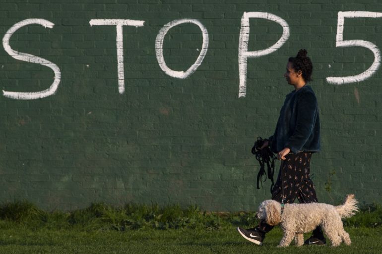 LONDON, UNITED KINGDOM - APRIL 10: A woman walks her dog in-front of graffiti saying 'Stop 5G' on April 10, 2020 in London, England. Public Easter events have been cancelled across the country, with the government urging the public to respect lockdown measures by celebrating the holiday in their homes. Over 1.5 million people across the world have been infected with the COVID-19 coronavirus, with over 7,000 fatalities recorded in the United Kingdom. (Photo by Justin Setterfield/Getty Images)