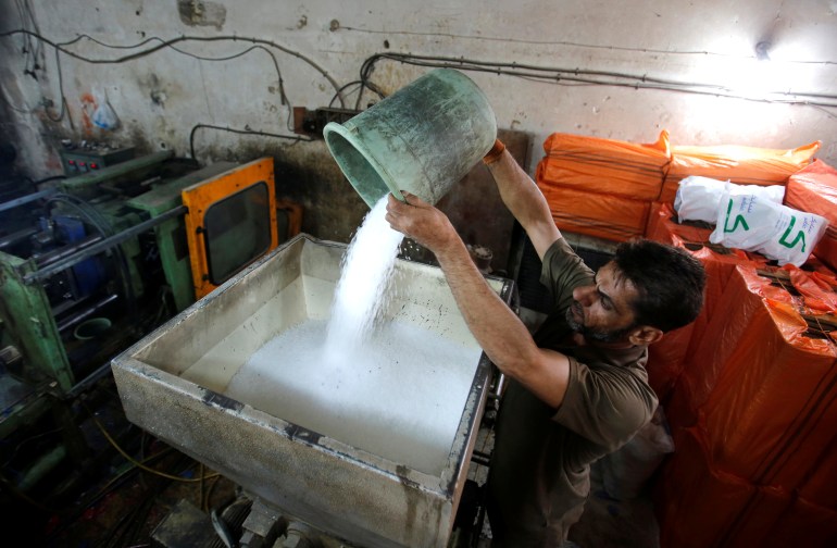 A worker puts plastic granules in a machine at a factory which manufactures plastic materials in Baghdad