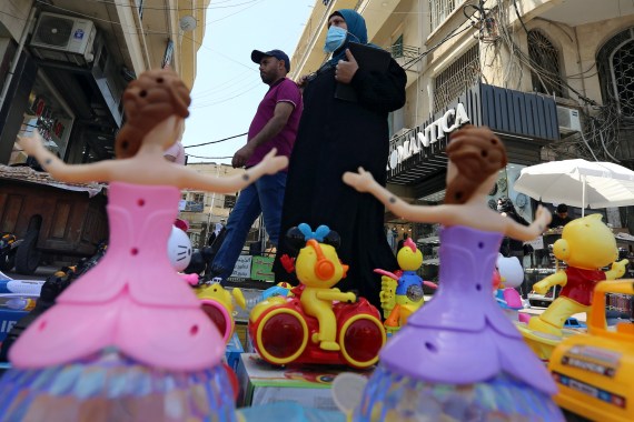 A woman wearing a face mask walks past toys for sale in Sidon