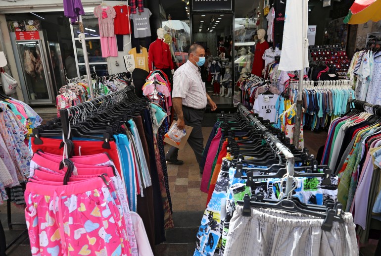 A man wearing a face mask walks past displayed clothing for sale