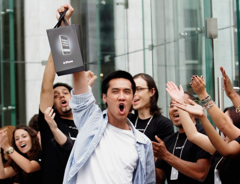 Surrounded by cheering Apple Store employees, one of the first iPhone buyers leaves the store on Fifth Avenue in New York