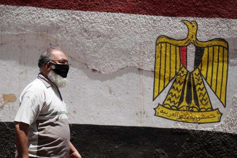 A man wearing a protective face mask to prevent the spread of the coronavirus disease (COVID-19) walks next to a wall painted with colors of Egypt's flag in downtown Cairo