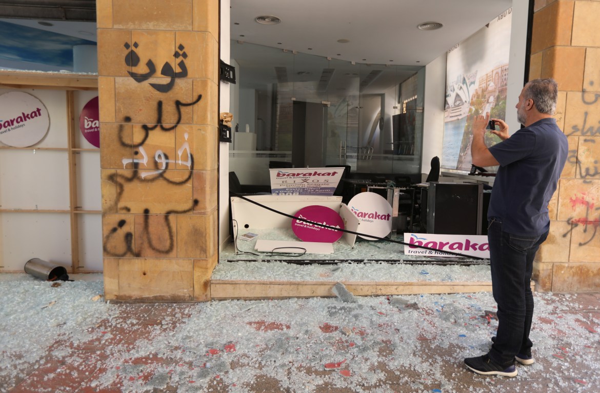 A man takes pictures of a damaged travel agency after overnight protests in Beirut