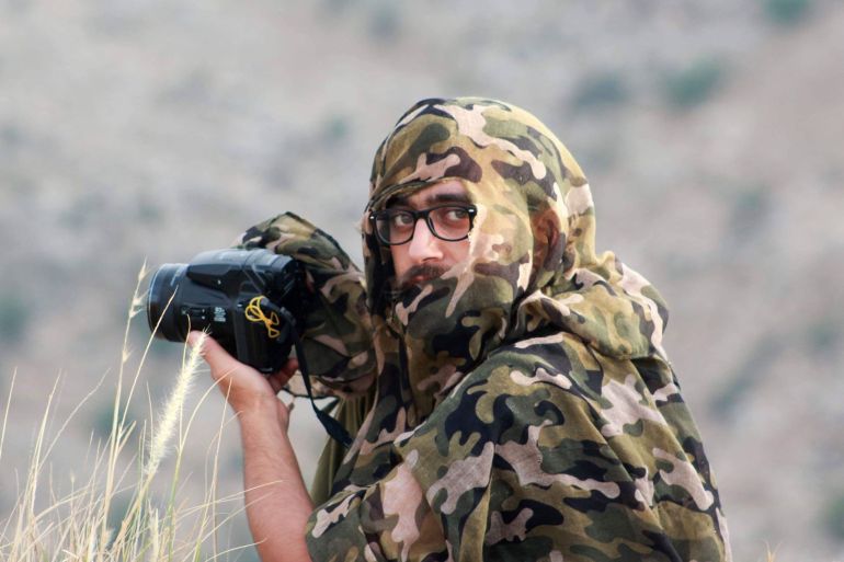 صورة لمحمد الشعيبي وهو في كمين يرتدي زيا يحاكي الطبيعة حوله، ويحمل كاميراته في دير غسانة شمال غرب رام الله وسط الضفة الغربية المحتلة.