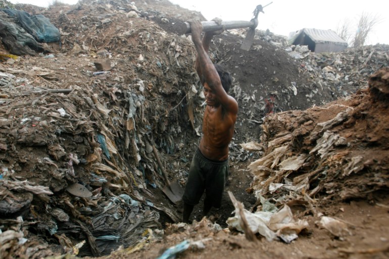 A man digs heap of garbage to recover copper and other metals from discarded electronic waste at Smokey Mountain in exchange of money at nearby junkshops along a road in Manila
