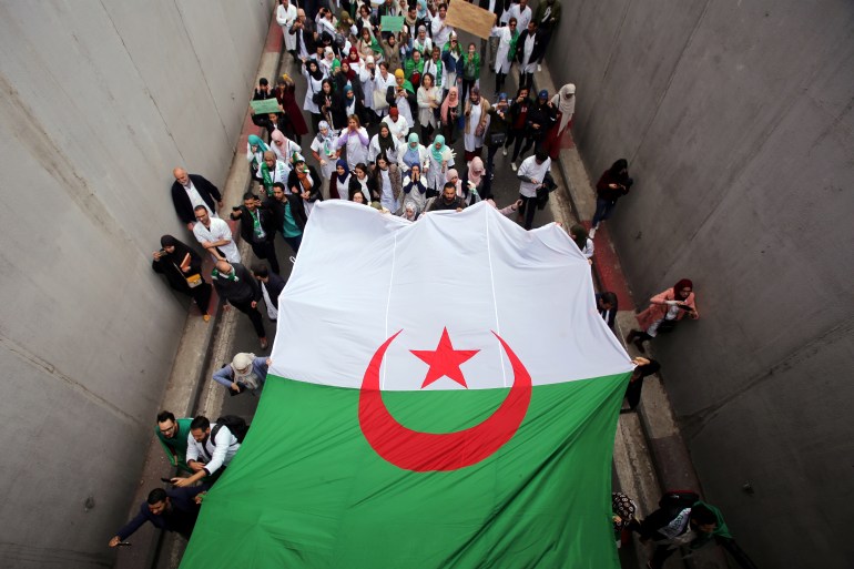 Health workers carry a national flag as they march during a protest calling on President Abdelaziz Bouteflika to quit, in Algiers