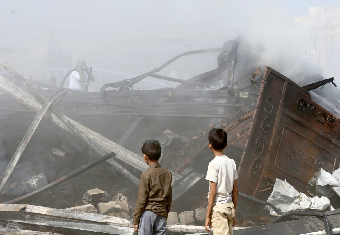 Boys look as a worker uses a hose to put down fire at a a vehicle oil and tires store hit by Saudi-led air strikes in Sanaa