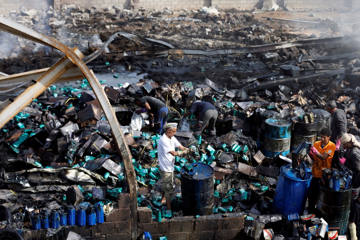 Workers salvage engine oil from the wreckage of a vehicle oil and tires store hit by Saudi-led air strikes in Sanaa