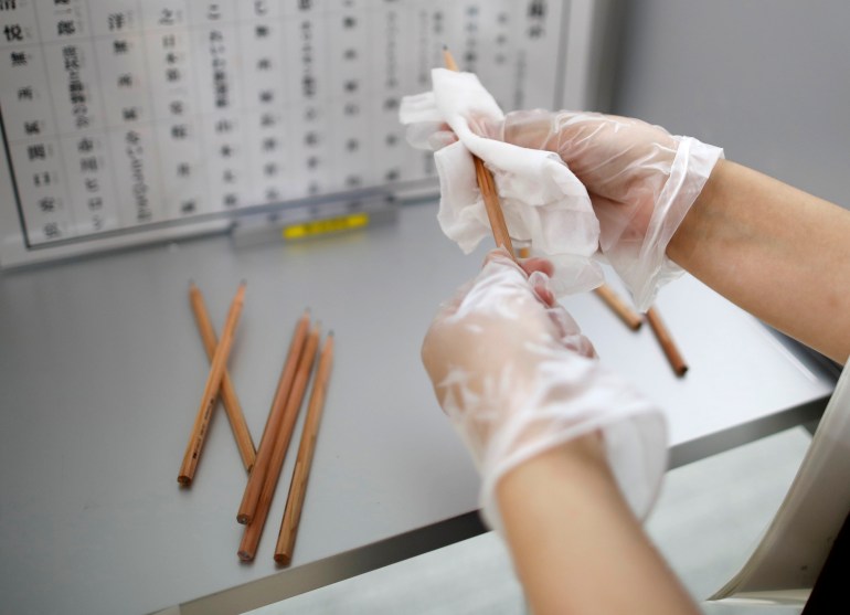 A member of Election Management Committee wearing vinyl gloves disinfects pencils for writing voting paper amid the coronavirus disease (COVID-19) outbreak, at a voting station for the Tokyo Governor election in Tokyo