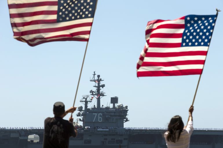 Supporters wave flags along shoreline as USS Ronald Reagan departs for Yokosuka, Japan from Naval Station North Island in San Diego