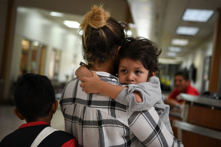 Paola, an asylum seeker from Honduras, carries four year-old son Jesse as they wait in a ticketing line with fellow migrant families recently released from detention at a bus depot in McAllen