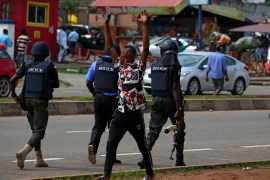 A man raising his arms walks past police officers as they disperse members of the IMN from a street in Abuja