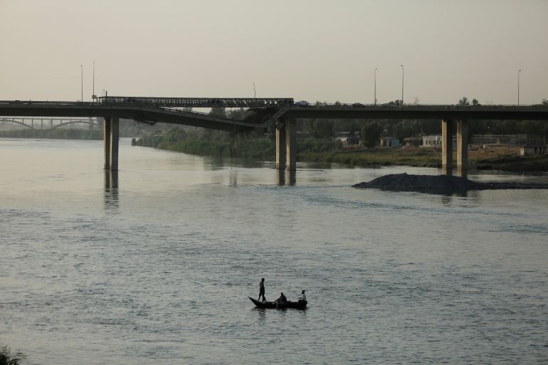 Iraqis cross the Tigris River by a boat near a bridge which was destroyed during the war against Islamic State militants in Mosul