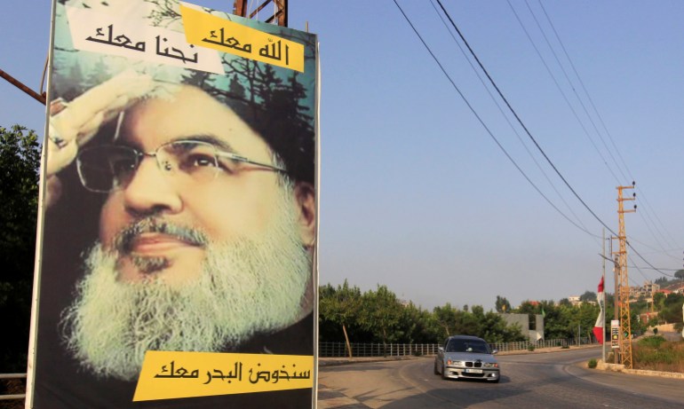 Car drives past a poster depicting Lebanon's Hezbollah leader Sayyed Hassan Nasrallah in Adaisseh village, near the Lebanese-Israeli border
