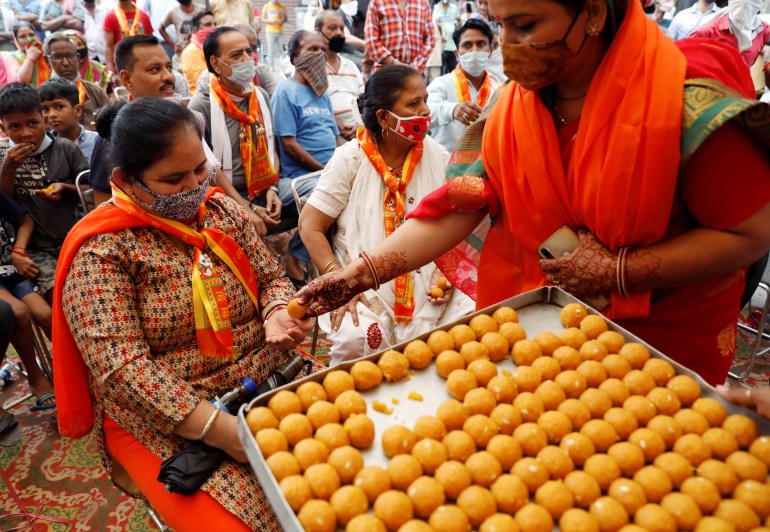 A woman distributes sweets during a live screening of the stone laying ceremony of the Ram Temple by Prime Minister Narendra Modi in Ayodhya, in New Delhi