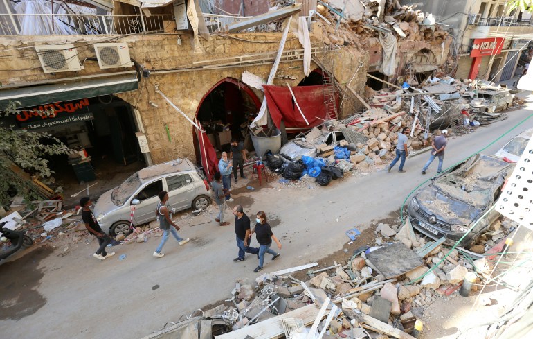 People walk near rubble and damaged vehicles following Tuesday's blast in Beirut's port area