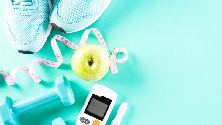 Healthy lifestyle, food and sport concept. Top view of diabetes tester set with athlete's equipment measuring tape green dumbbell, sport water bottles, fruit on bright green pastel background.