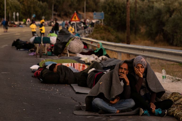 Couple sits covered with a blanket as refugees and migrants camp on a road following a fire at the Moria camp on the island of Lesbos