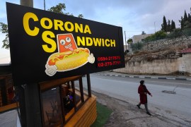 A woman walks past the "Corona Sandwich" restaurant in the occupied West Bank town of Bethlehem, owned by a former Palestinian tourist guide, on November 6, 2020. - When the coronavirus pandemic left Bethlehem without its hordes of visitors, tour guide Raed Bannura needed a new source of income. Located in the shadow of the Church of Nativity basilica, Bannura's small cafeteria is easily spotted by its huge red and yellow "Corona Sandwich" sign. (Photo by Emmanuel DUNAND / AFP)
