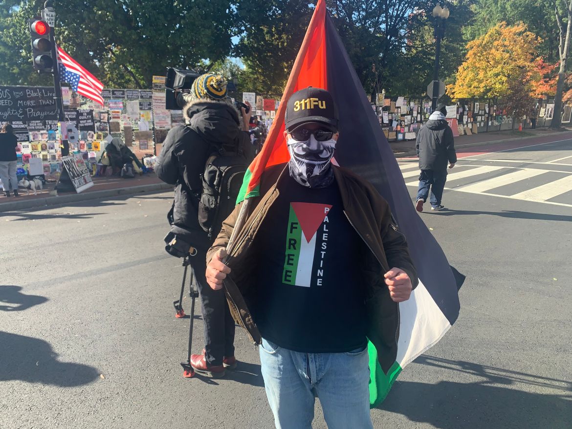 متظاهر أميركي يرتدي صورة علم ويحمل علم فلسطين خارج حواجز البيت الأبيض