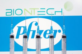 Syringes are seen in front of displayed Biontech and Pfizer logos in this illustration
