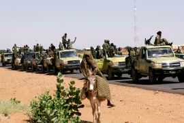 Military convoy of government forces passes a woman on a donkey, on their way to Tabit village in North Darfur
