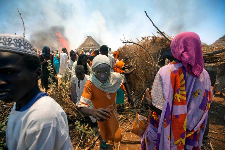 Women and children run away with their belongings from a fire in Kuma Garadayat, a village located in North Darfur