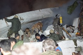 Israeli emergency workers assisted by two dogs go through the rubble of a collapsed residential building