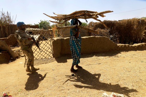 A peacekeeper from the UN Hybrid Operation in Darfur (UNAMID) escorts an internally displaced Sudanese woman carrying firewood on her head as she walks within the Kalma camp for internally displaced persons (IDPs) in Darfur