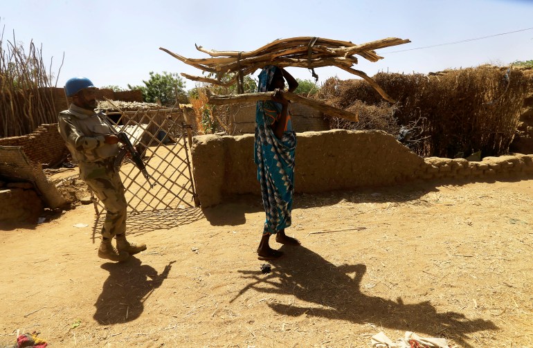 A peacekeeper from the UN Hybrid Operation in Darfur (UNAMID) escorts an internally displaced Sudanese woman carrying firewood on her head as she walks within the Kalma camp for internally displaced persons (IDPs) in Darfur
