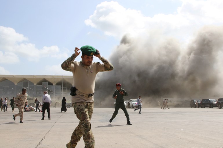 A security personnel member reacts as dust rises after explosions hit Aden airport, upon the arrival of the newly-formed Yemeni government in Aden