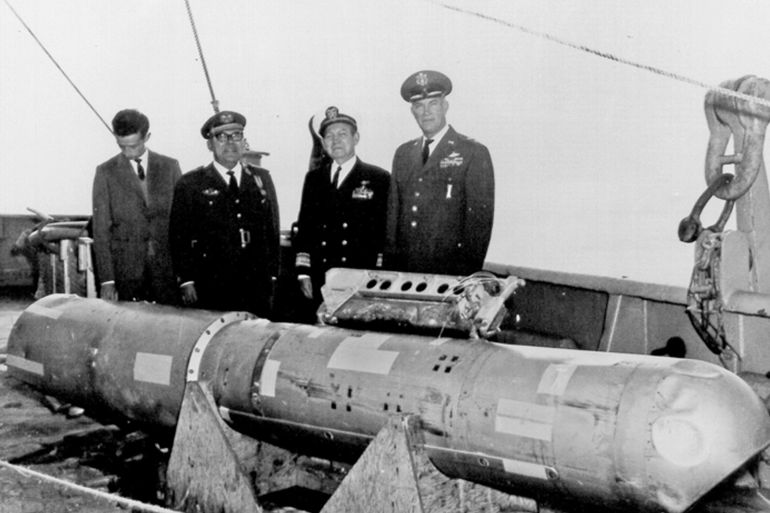 Eighty days after it fell into the ocean following the January 1966 midair collision between a nuclear-armed B-52G bomber and a KC-135 refueling tanker over Palomares, Spain, this B28RI nuclear bomb was recovered from 2,850 feet (869 meters) of water and lifted aboard the USS Petrel (note the missing tail fins and badly dented "false nose"). This photograph was among the first ever published of a U.S. hydrogen bomb. Left to right are Sr. Don Antonio Velilla Manteca, chief of the Spanish Nuclear Energy Board in Palomares; Brigadier General Arturo Montel Touzet, Spanish coordinator for the search and recovery operation; Rear Admiral William S. Guest, commander of U.S. Navy Task Force 65; and Major General Delmar E. Wilson, commander of the Sixteenth Air Force. The B28 had a maximum yield of 1.45 megatons.