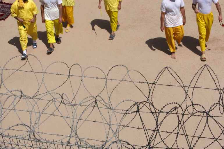 Detainees pass the time as they seen behind wire at Camp Bucca in southern Iraq