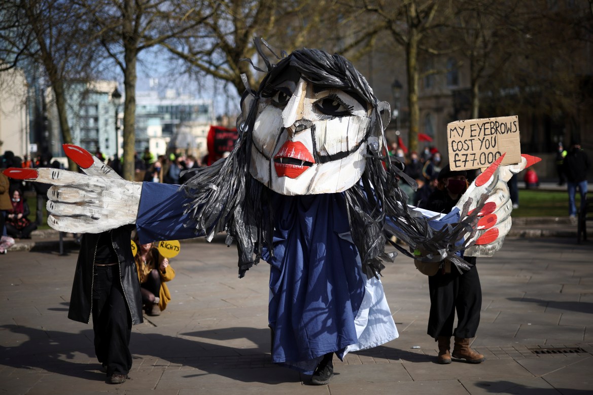Un manifestant portant un masque porte une pancarte indiquant: "Mon bandeau vous coûte 77 000 livres" (Reuters)