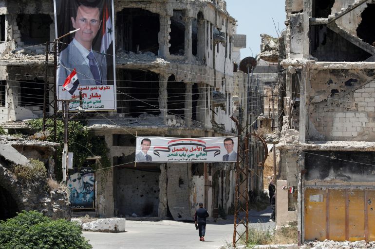A man walk past banners depciting Syria's President Bashar al-Assad, near damaged buildings in Homs