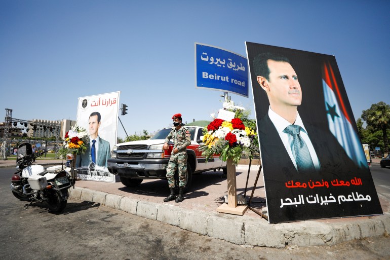 A Syrian military police officer stands near posters depicting Syria's President Bashar al-Assad, during the country's presidential elections in Damascus