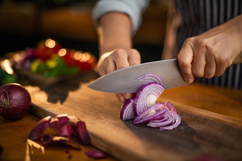 chef is precisely slicing red onions on a wooden cutting board