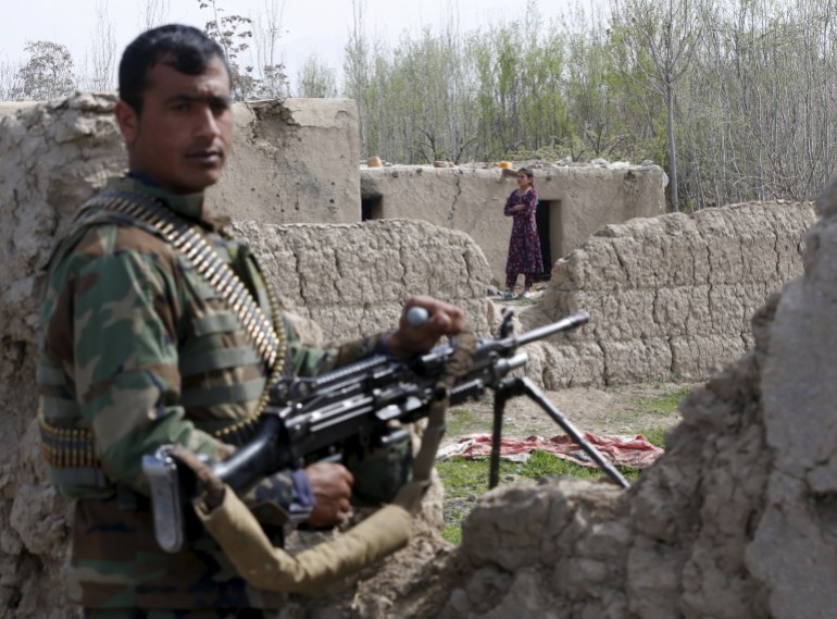 Afghan National Army (ANA) soldier keeps watch as a young girl stands in front of her house in Dand Ghori district of Baghlan
