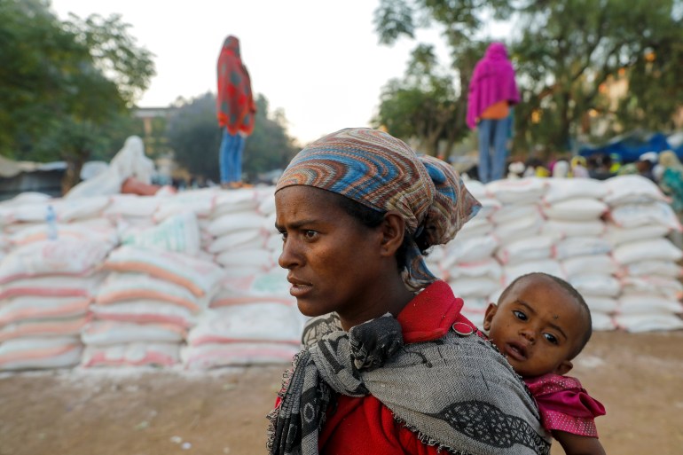 A woman carries an infant as she queues in line for food, at the Tsehaye primary school, which was turned into a temporary shelter for people displaced by conflict, in the town of Shire, Tigray region, Ethiopia, March 15, 2021. Picture taken March 15, 2021. REUTERS/Baz Ratner