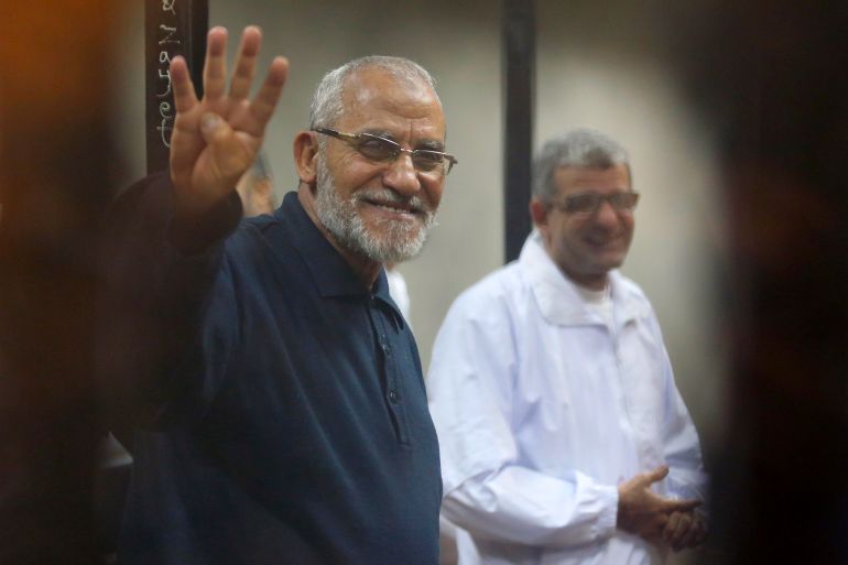 Muslim Brotherhood's Supreme Guide Mohamed Badie flashes the Rabaa sign as he stands behind bars during his trial with ousted Egyptian President Mohamed Mursi and other leaders of the brotherhood at a court on the outskirts of Cairo