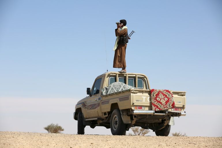 Tribal fighter loyal to Yemen's government stands on the roof of a pick-up truck as he uses binoculars to look at at Houthi positions in an area between Yemen's northern provoices of al-Jawf and Marib