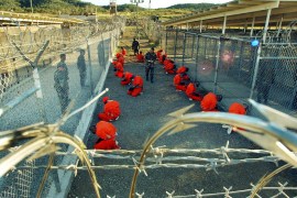In this photo released 18 January 2002 by the Department of Defense, Al-Qaeda and Taliban detainees in orange jumpsuits sit in a holding area under the surveillence of US military police at Camp X-Ray at Naval Base Guantanamo Bay, Cuba, during in-processing to the temporary detention facility 11 January 2002. The detainees, captured in Afghanistan during Operation Enduring Freedom, are given a basic physical exam by a doctor, to include a chest x-ray blood samples drawn to assess their health. AFP PHOTO / US NAVY / Shane T. McCOY (Photo by - / DOD / US NAVY / AFP) (Photo by -/DOD / US NAVY/AFP via Getty Images)