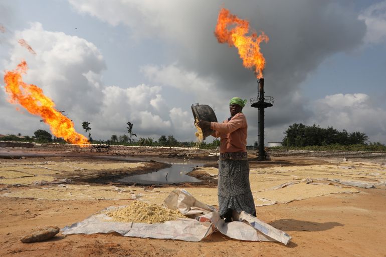 A woman empties a plastic bowl filled with tapioca close to a gas flaring furnace in Ughelli, Delta State
