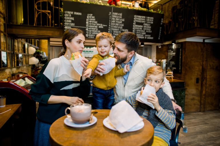 Family having breakfast at city cafe with blurred interior on the background. Adorable children and their parents eating fresh tasty croissants and drinking cocoa drink or coffee; Shutterstock ID 1750438055; purchase_order: aljazeera net; job: ; client: ; other: