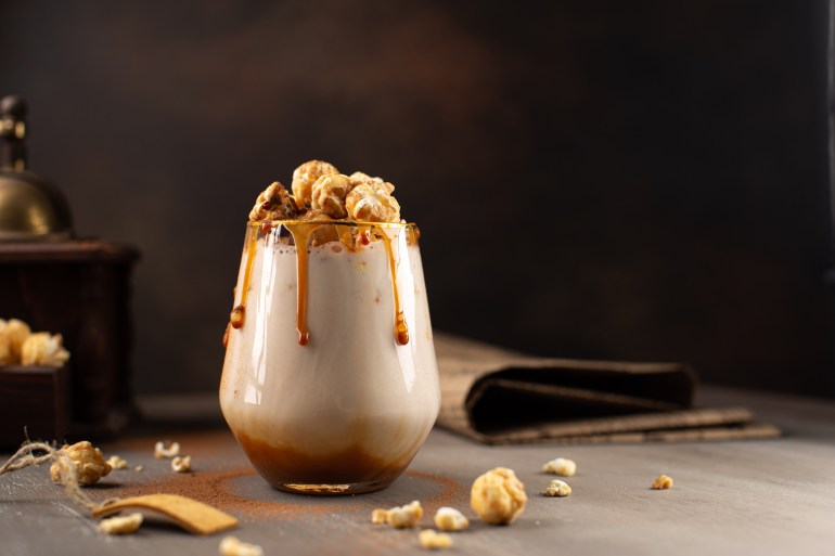 Sweet Milkshake with caramel syrup,cream liqueur,caramel popcorn and chocolate powder on brown background with vintage,manual coffee grinder.; Shutterstock ID 1912759621; purchase_order: aljazeera net; job: ; client: ; other:
