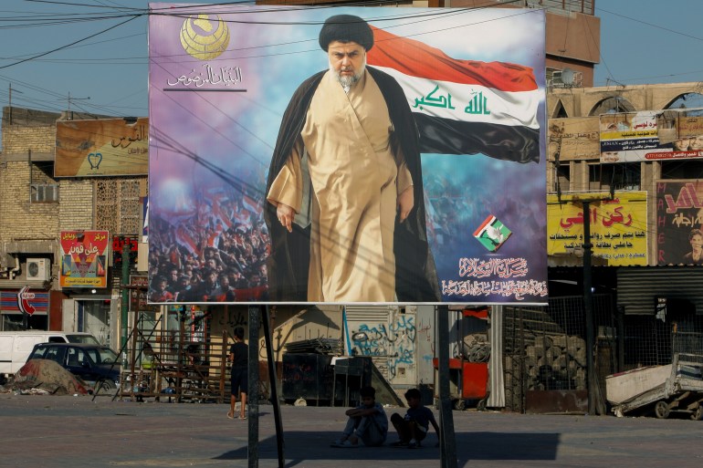 Iraqi boys sit under a poster of Iraqi Shi'ite cleric Moqtada al-Sadr in the Sadr City district of Baghdad