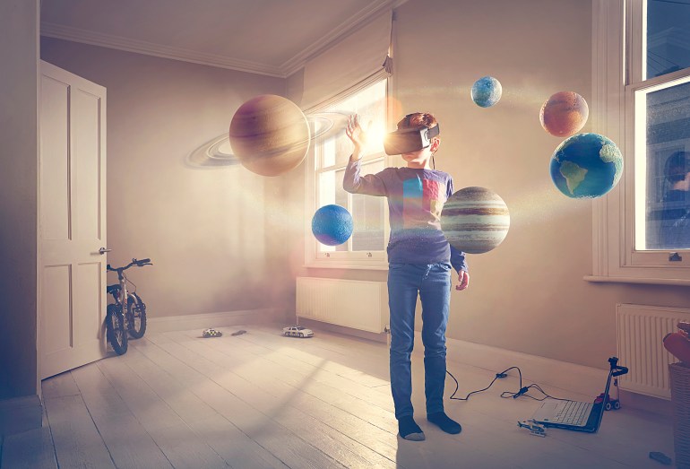 مجموعة الكواكب الشمسية - غيتي A boy wears a virtual reality headset gazing in wonder into a virtual solar system that has taken over his bedroom.