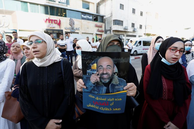Demonstrators, of which one is holding a placard, protest over the death of Nizar Banat, a critic of the Palestinian Authority, in Hebron, in the Israeli-occupied West Bank, June 27, 2021. The placard reads, "This country deserves you to sacrifice, raise your voice and don't be afraid". REUTERS/Mussa Qawasma