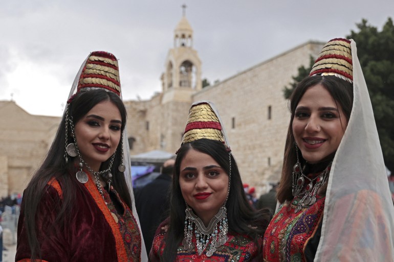 Palestinian women, wearing traditional clothing, pose for a picture outside the Church of the Nativity, revered as the site of Jesus Christ's birth, during Christmas celebrations in the biblical city of Bethlehem in the Israeli-occupied West Bank, on December 24, 2021. (Photo by ABBAS MOMANI / AFP)